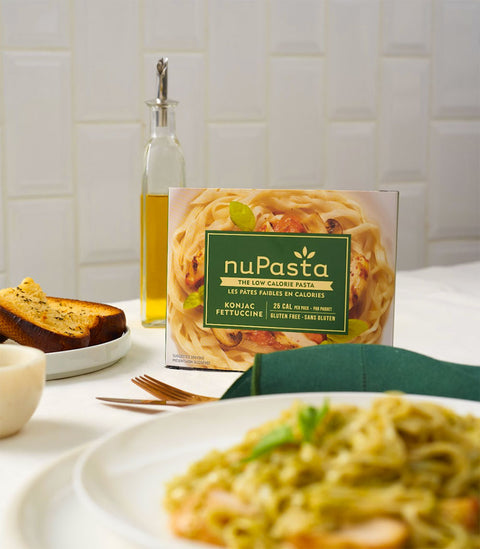 Box of nuPasta Fettuccine with a plate of pasta and bread on a table.