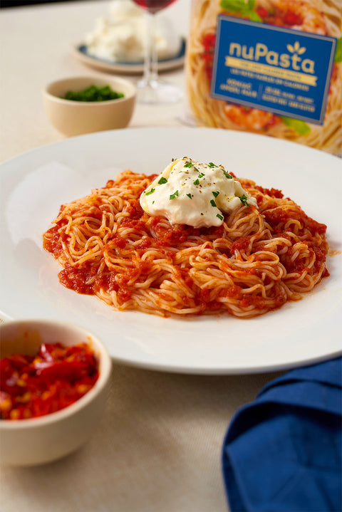 Spaghetti dish with creamy sauce on a white plate, featuring nuPasta Angel Hair  packaging in the background.