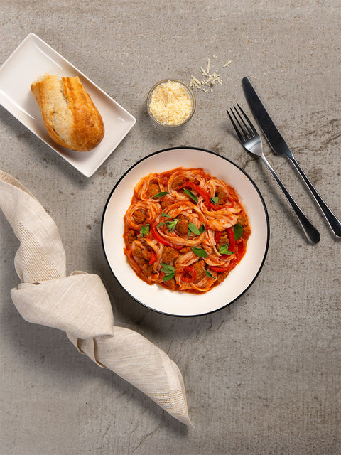 Keto vodka sauce with sausage with a bread roll, fork, and knife on a gray surface made with nuPasta noodles
