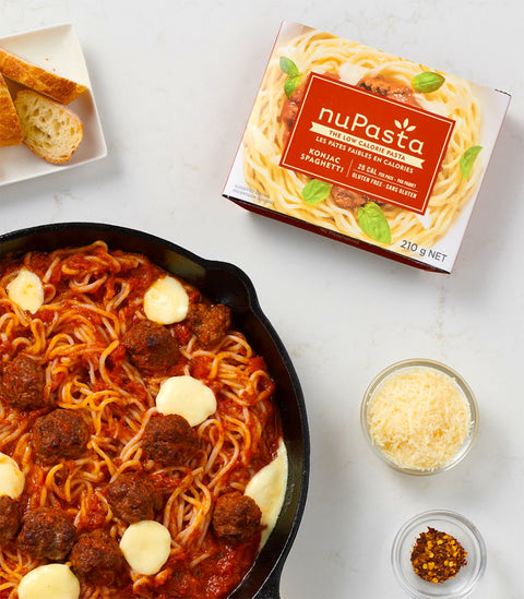 Spaghetti with meatballs in a skillet next to a box of nuPasta spaghetti on a white surface.